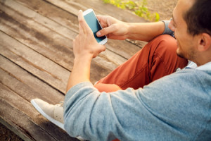 31821914 - young  hipster man using smart phone sitting on wooden boards